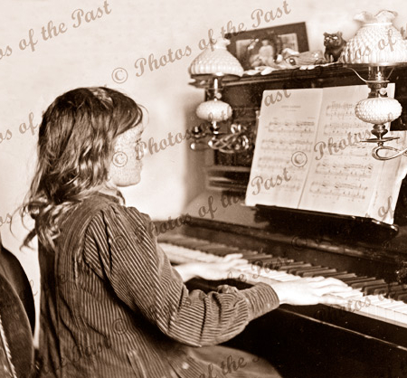 Young girl playing a candalabra fitted piano.