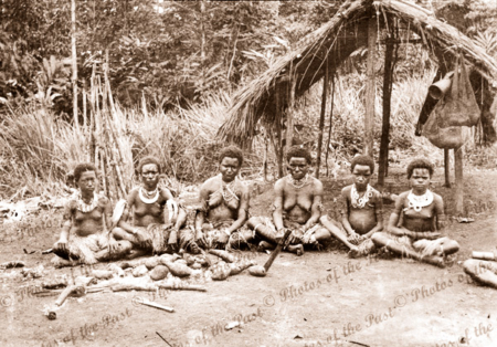 Six Papuan women & girls sitting on ground with yams. Papua New Guinea