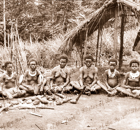Six Papuan women & girls sitting on ground with yams. Papua New Guinea