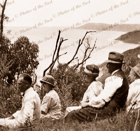 Mixed group sitting on hillside at Big Hill, Great Ocean Road, Victoria. Lorne in distance. c1920s