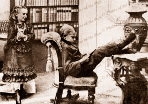 A man of learning. Boy with feet up reading a book. Admirer looks on. c1900